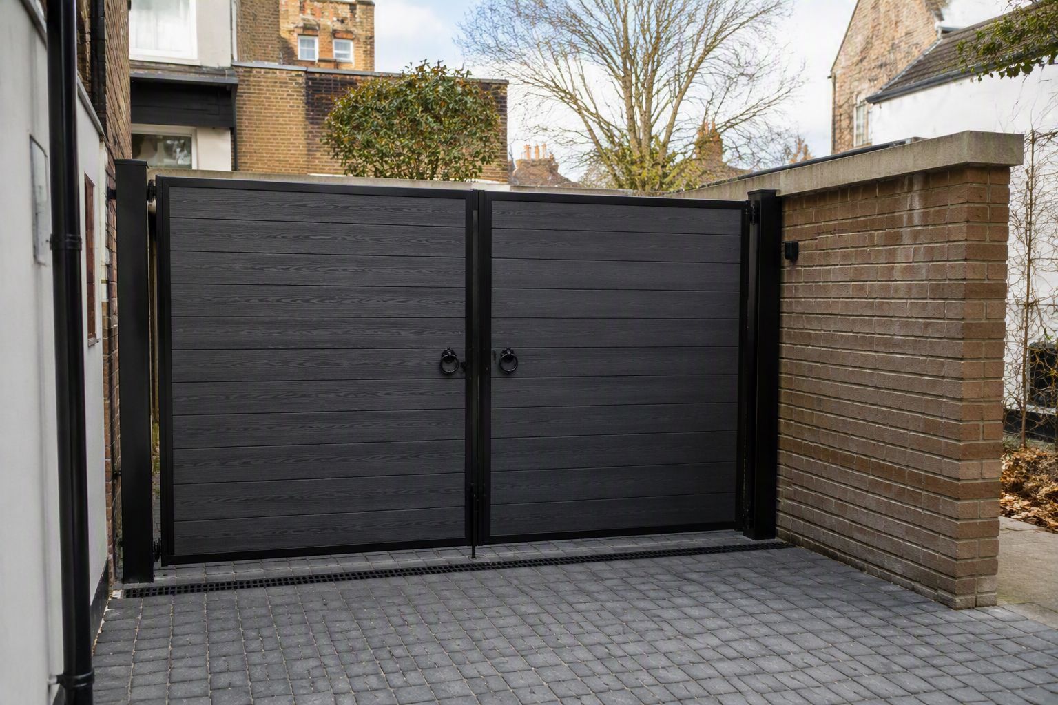 A pair of bespoke dark driveway gates hung between masonry piers
