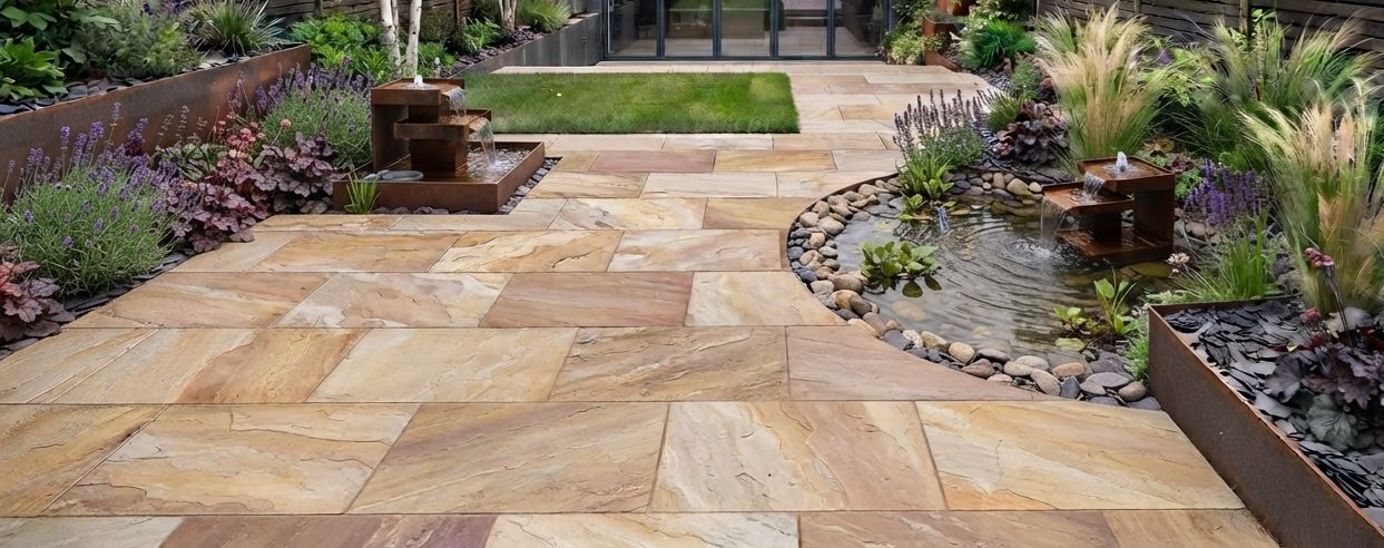 Warm toned natural sandstone patio beside a water feature and planted border